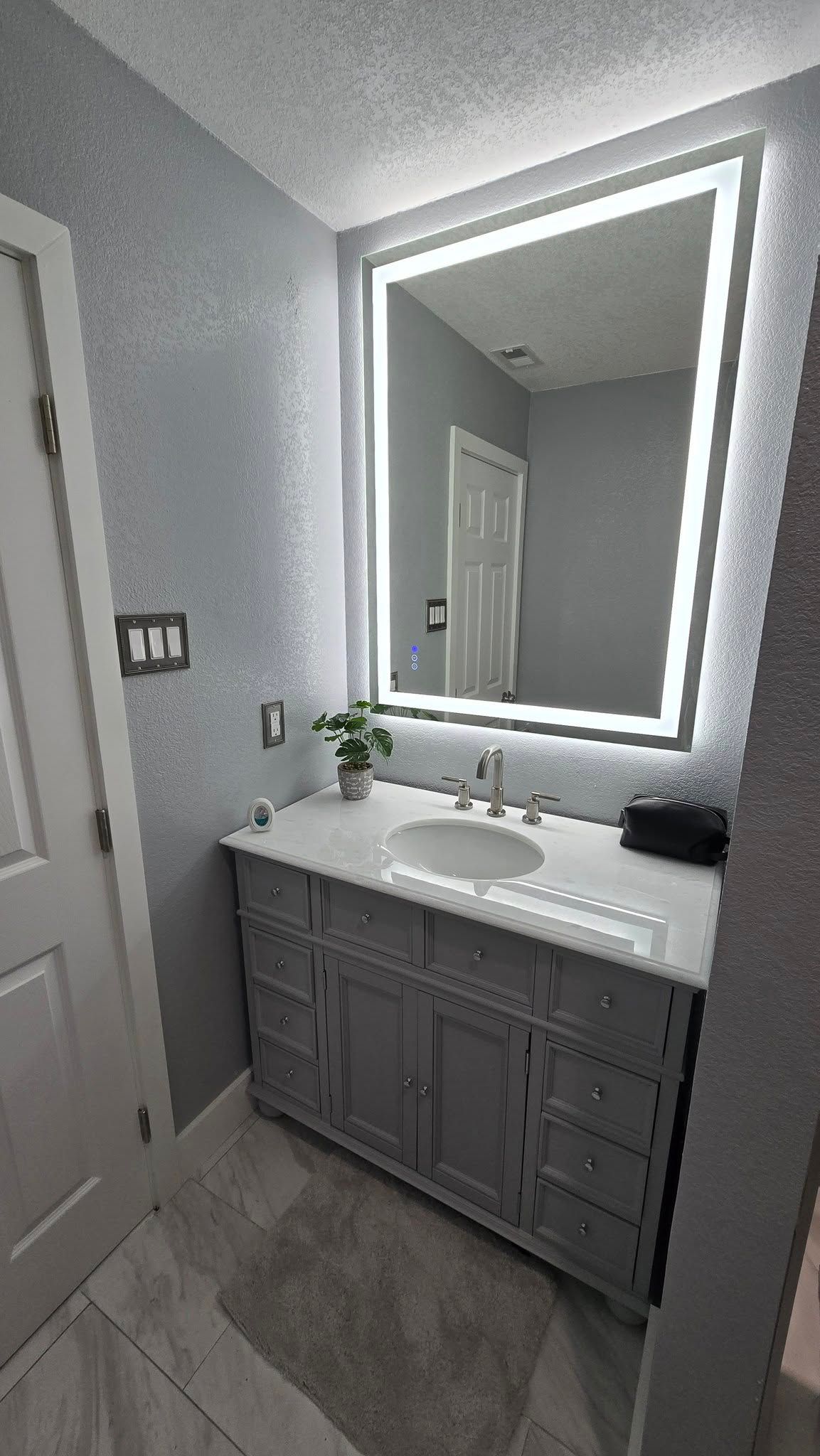 Bathroom with a lighted mirror above a gray vanity, white countertop, and gray walls.