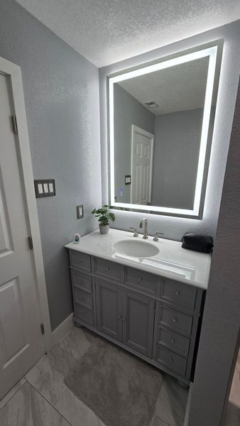 Bathroom with a lighted mirror above a gray vanity, white countertop, and gray walls.