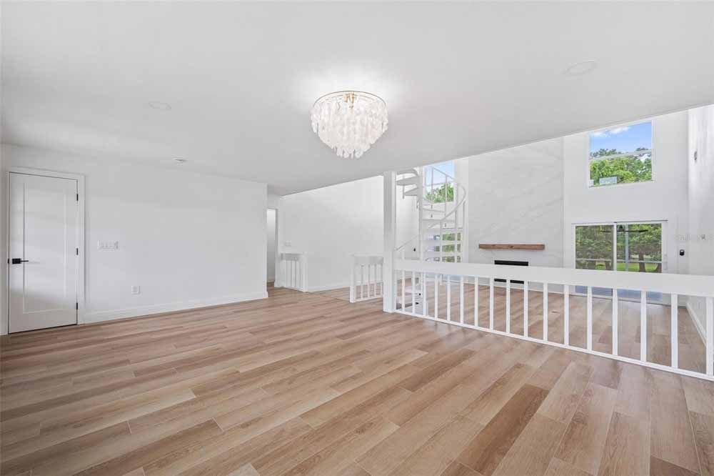Empty bright living room with hardwood floors, white walls, chandelier, and a large window.