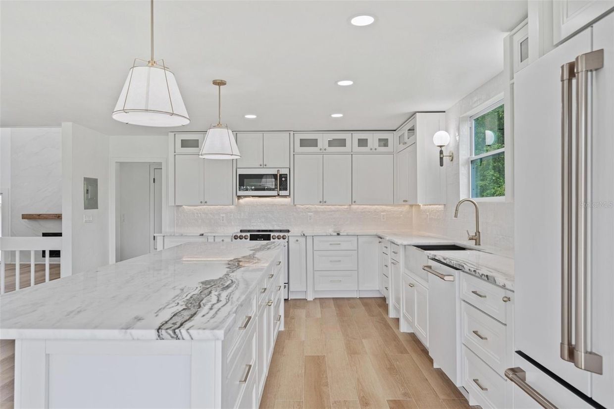 White kitchen with marble countertops, light wood floors, and pendant lighting.