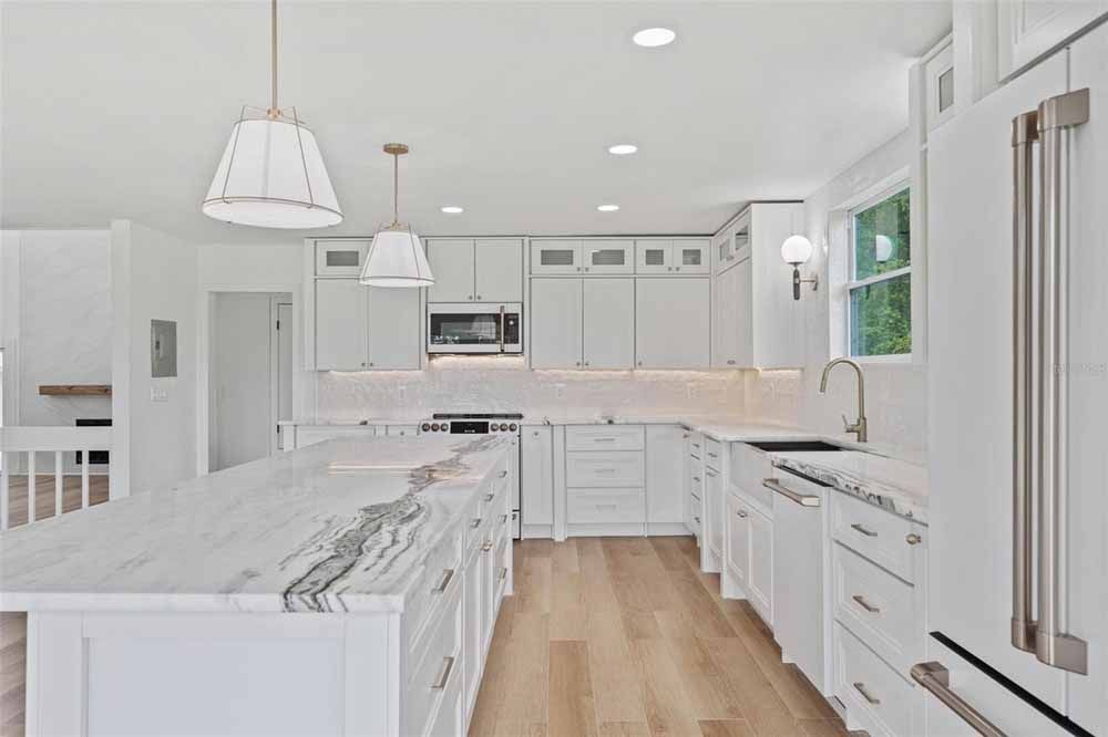 White kitchen with marble countertops, wood floors, and pendant lights.