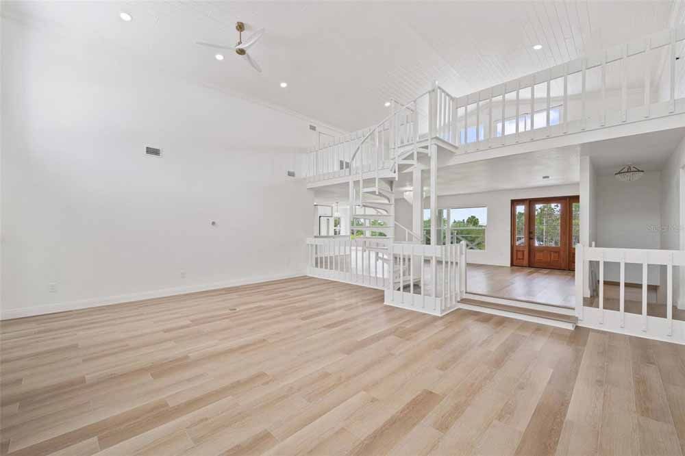 Spacious white interior with light wood floors, a spiral staircase to a loft, and large windows.