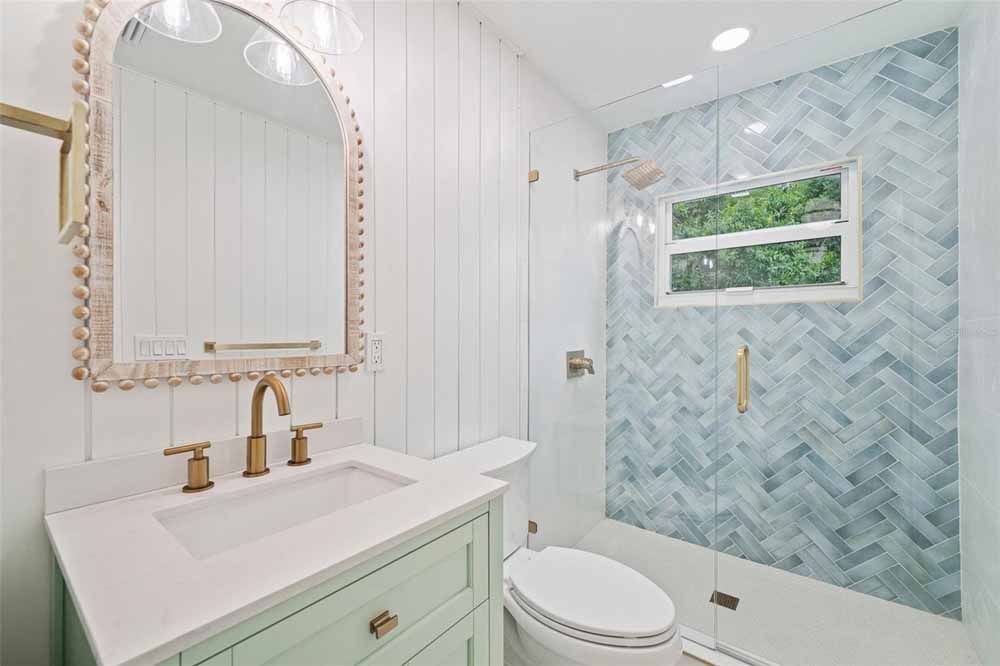 Bathroom with aqua vanity, gold fixtures, white walls, and blue tile shower.