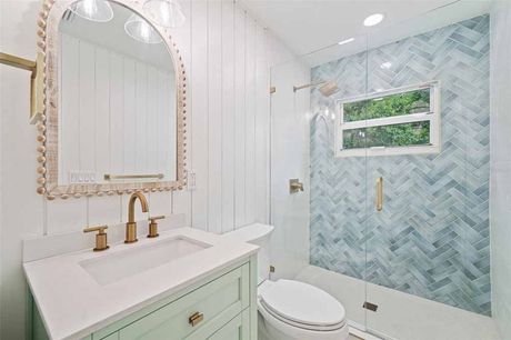 A bright bathroom with a mint-green vanity, gold fixtures, white walls, and a blue tile shower.