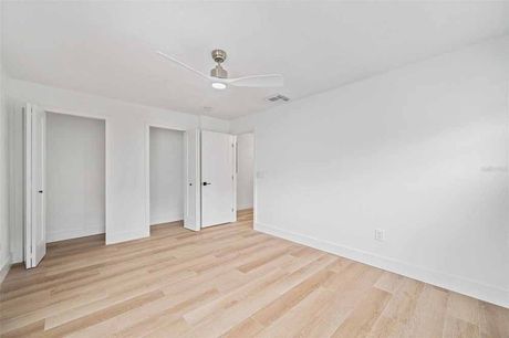 Empty room with light wood floors, white walls, and closet doors. A ceiling fan is visible.