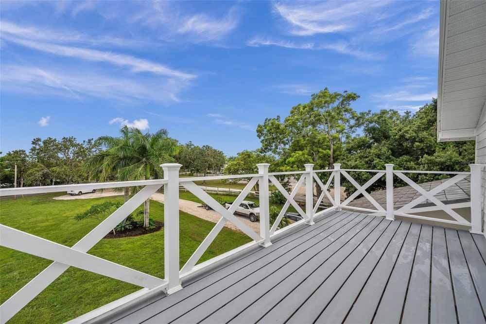 Balcony with gray decking, white railing, and a view of green trees and blue sky.