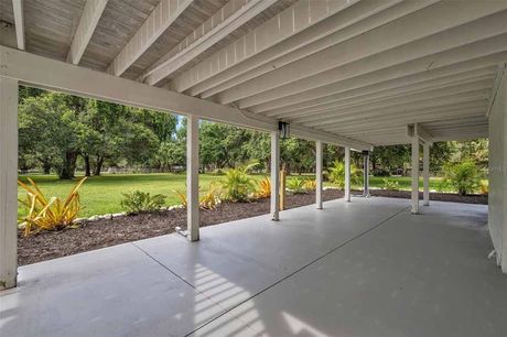 Covered patio with gray floor, white posts, and green lawn in the background.