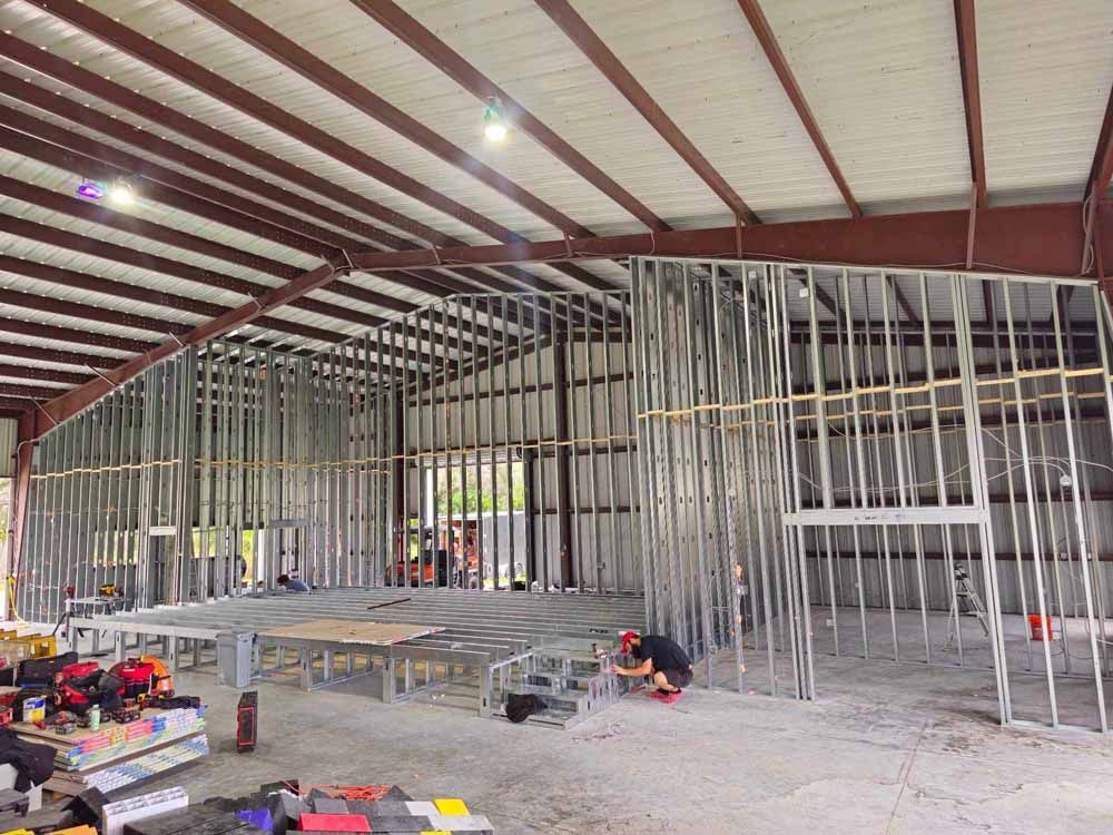 Interior of a steel building under construction; metal studs frame walls and an employee works on the floor.
