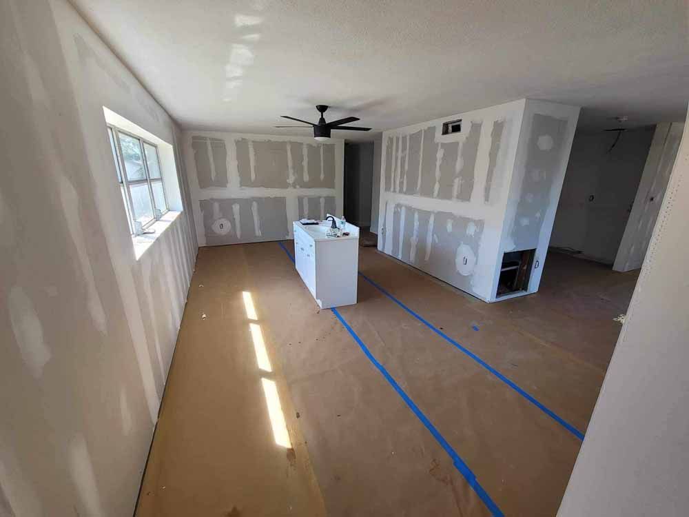 Interior room under renovation with drywall installed; a white cabinet, window, and brown floor covering.