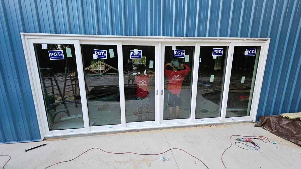White framed sliding glass door with a person in red shirt, blue building background.