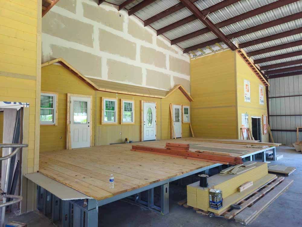 A yellow stage set of a house, inside a large warehouse under construction.