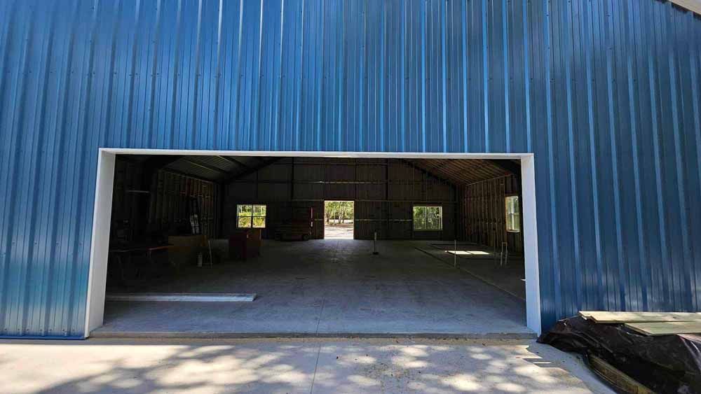 Blue metal building with large open doorway. Interior visible with concrete floor, and windows.