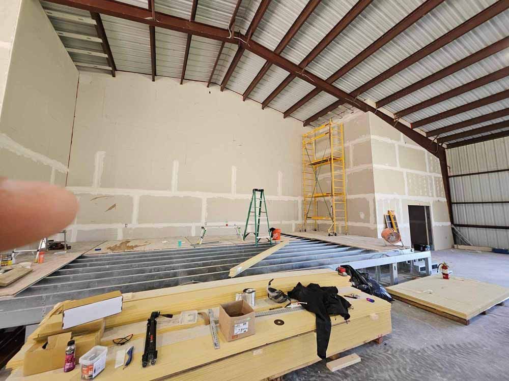 Interior construction site with drywall on walls and ceiling, metal beams, and construction materials.