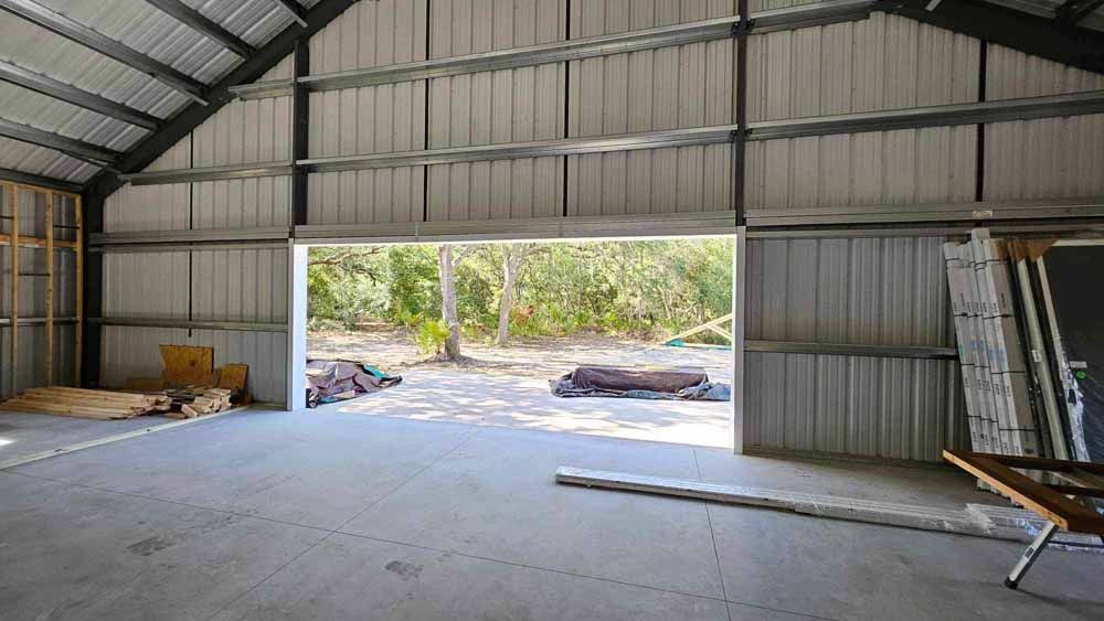 Interior of a metal building with an open doorway to a wooded area. Concrete floor, metal walls and roof.
