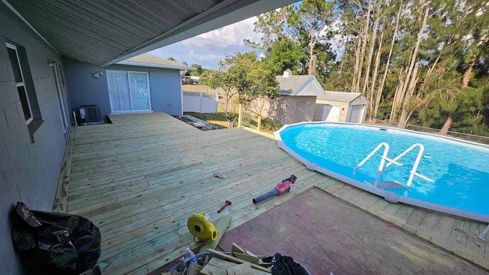 Backyard with pool, deck, and house. A person lies on the deck near tools and a pool.