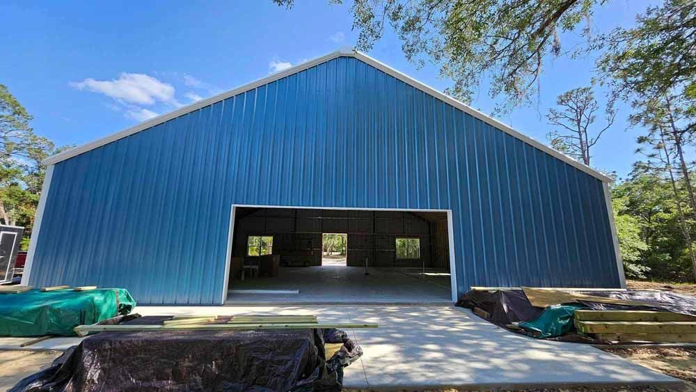 Blue metal barn with large open doorway, concrete pad in front, bright blue sky.