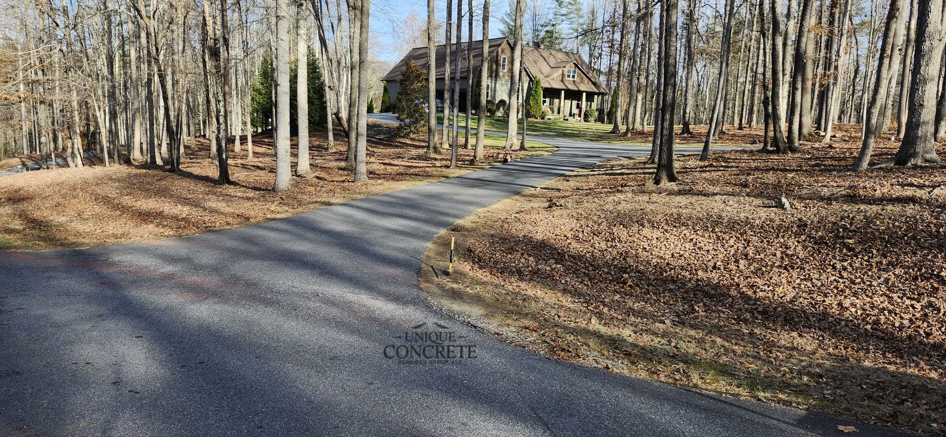 A gravel road curves through bare trees toward a house in a wooded setting.