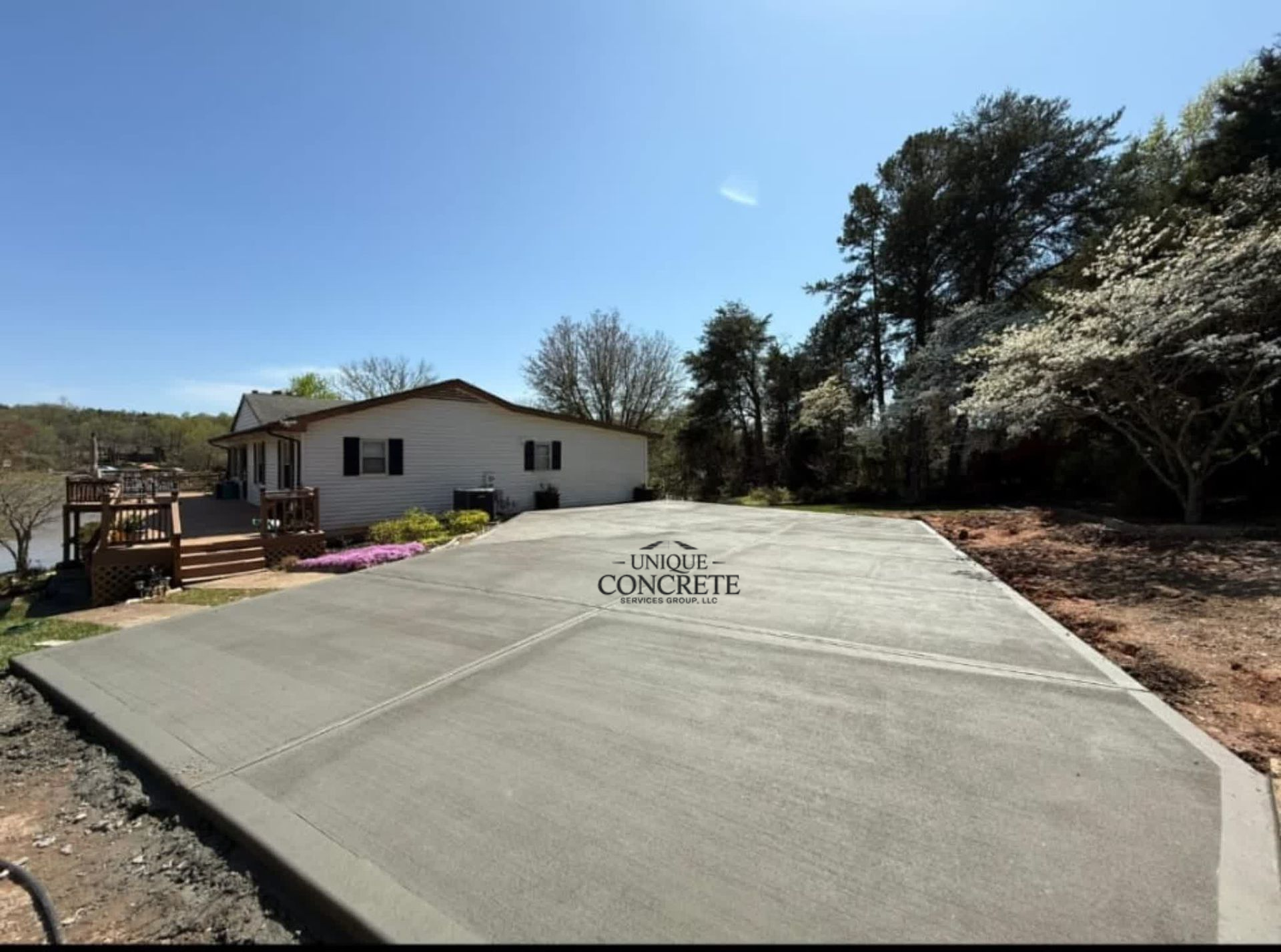 Newly poured concrete driveway in front of a white house, against a backdrop of trees and blue sky.