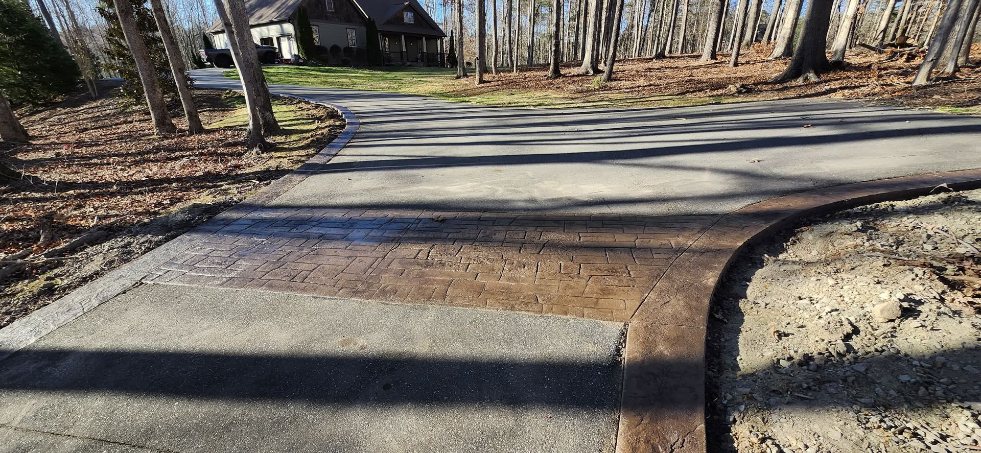 Asphalt driveway with a house in the background, trees on the side, and fallen leaves.