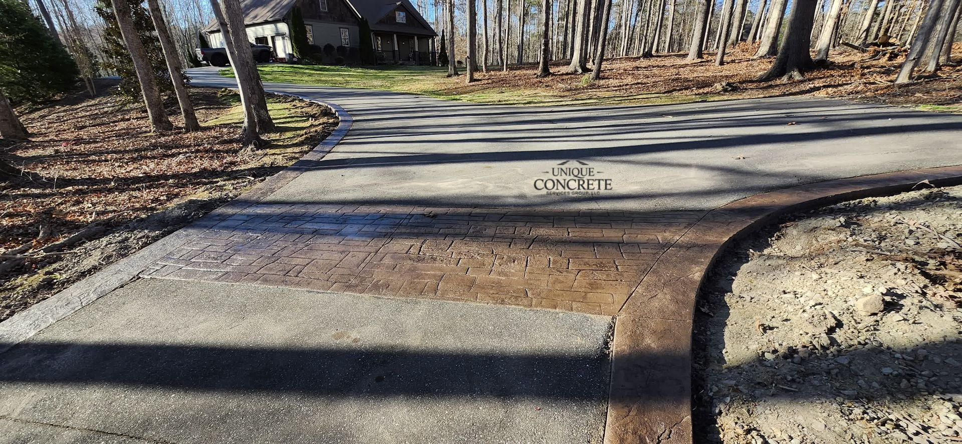Asphalt driveway with a house in the background, trees on the side, and fallen leaves.