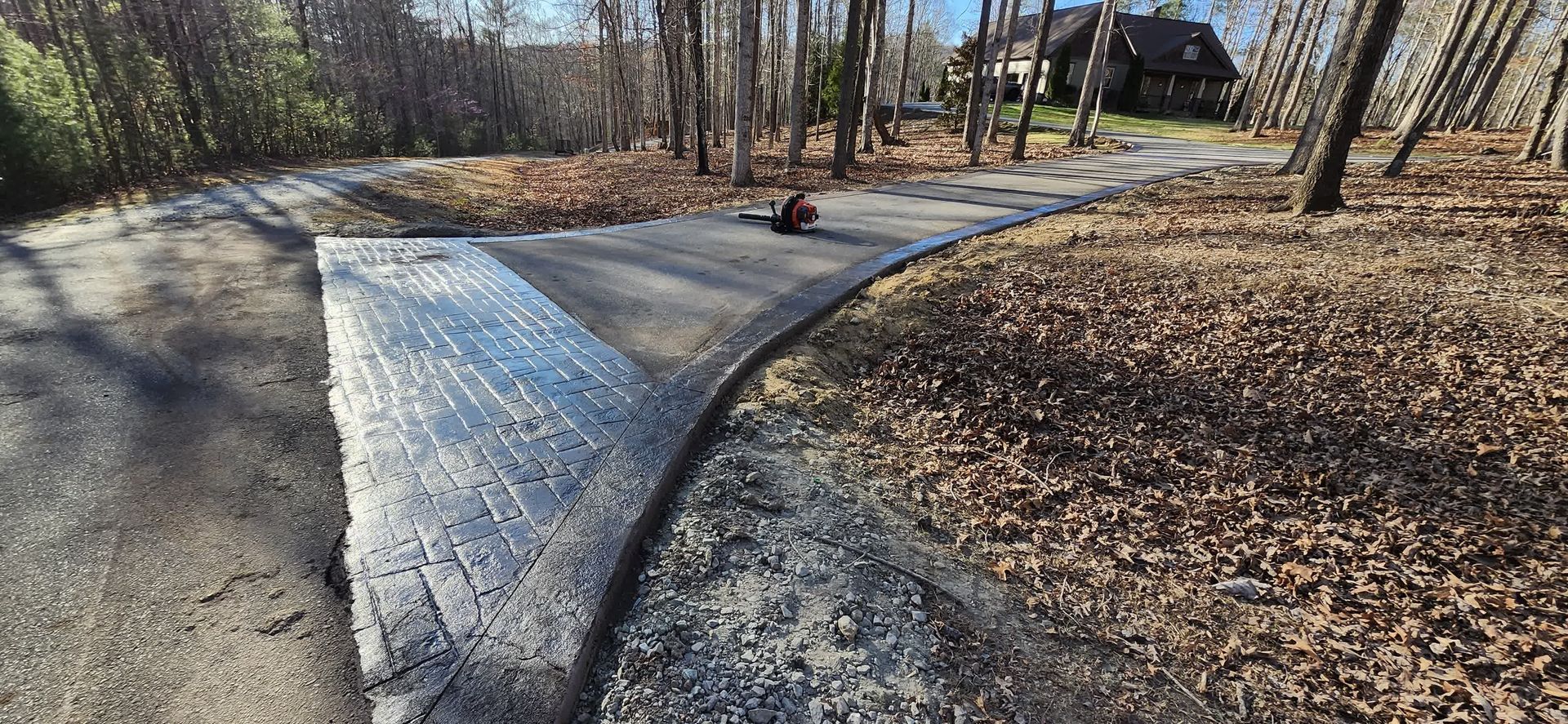 Newly paved pathway curving through a wooded area, leading towards a house.