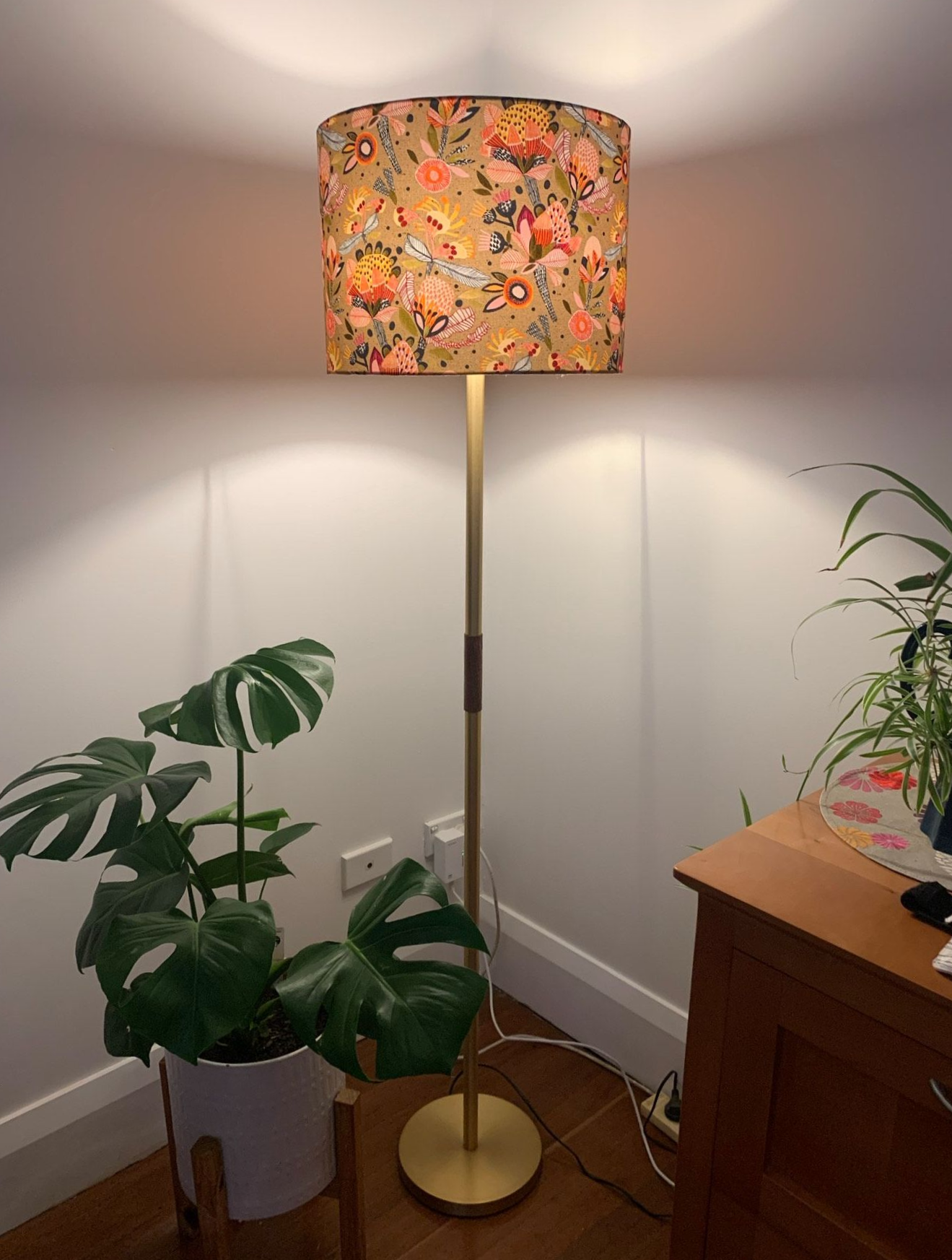 Floor lamp with floral lampshade, next to a Monstera plant and wooden cabinet— Brightway Lighting in Lismore, NSW
