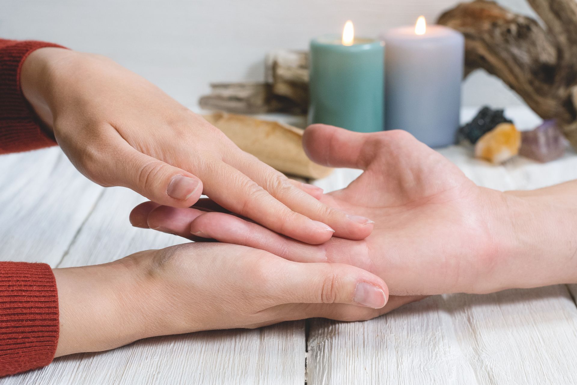 A person is holding another person 's hand on a table with candles in the background.