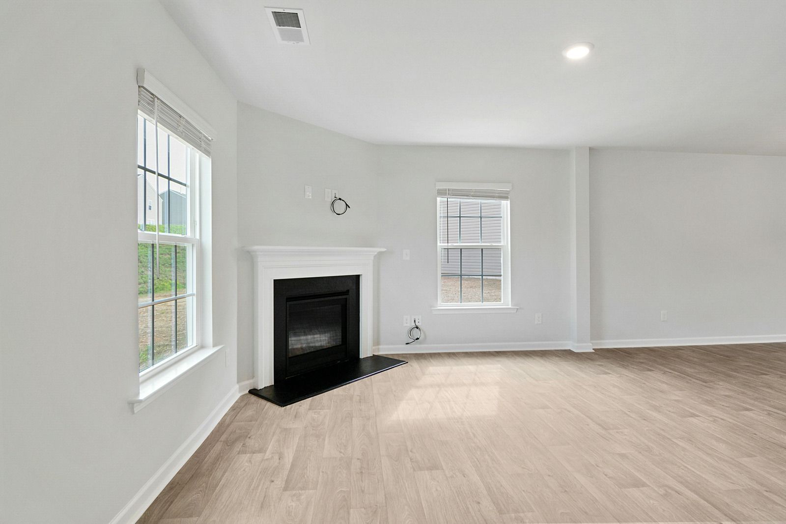 Empty white living room with two windows, light wood floors, and a black fireplace