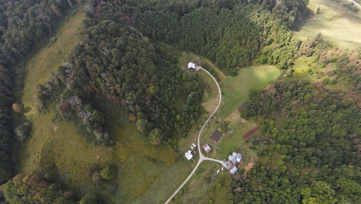 Aerial view of a winding road and buildings nestled in a forested, hilly landscape.