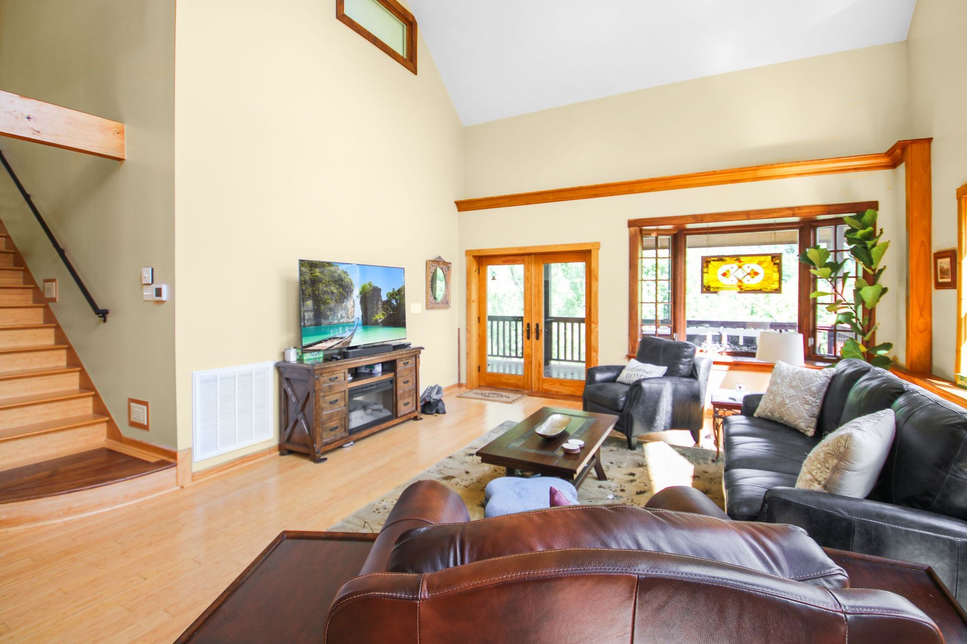 Living room with hardwood floors, leather sofas, TV, and a view through French doors.
