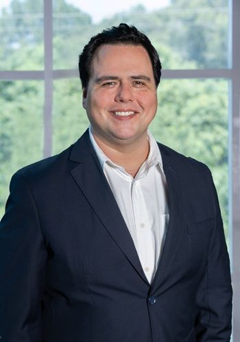 Un hombre con traje y camisa blanca está parado frente a una ventana.