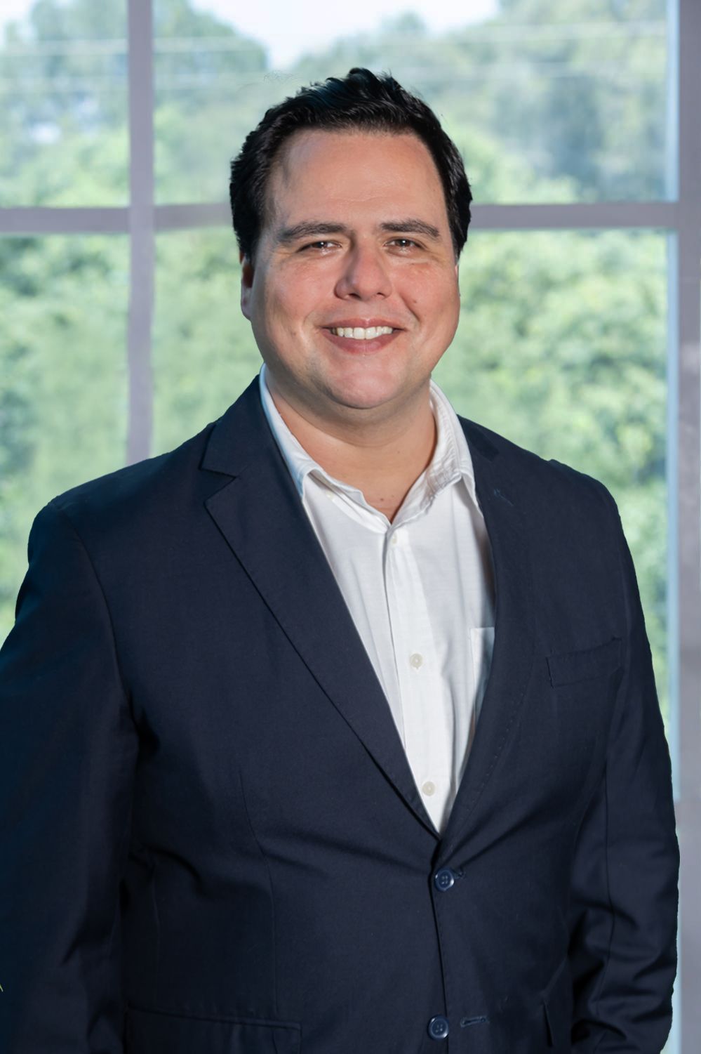 Un hombre con traje azul y camisa blanca está parado frente a una ventana.