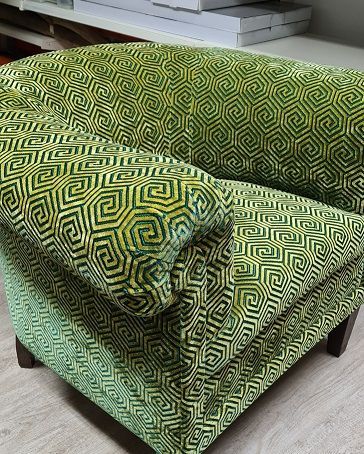 Auf einem Holzboden steht ein grüner Stuhl mit einem gelben Muster.