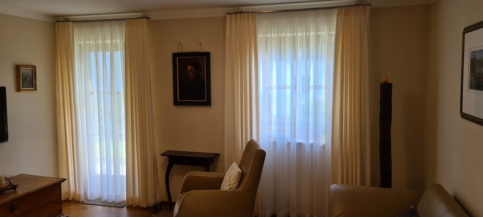 Ein Wohnzimmer mit Couch, Sessel, Tisch und zwei Fenstern.