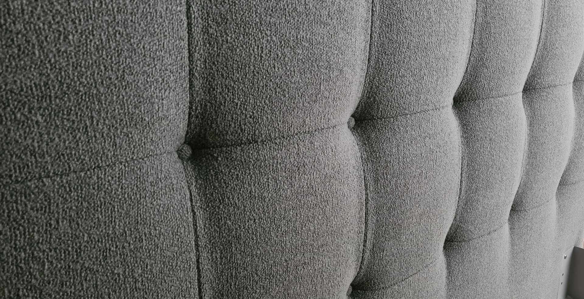 Eine Nahaufnahme eines grauen, gepolsterten Kopfteils auf einem Bett.