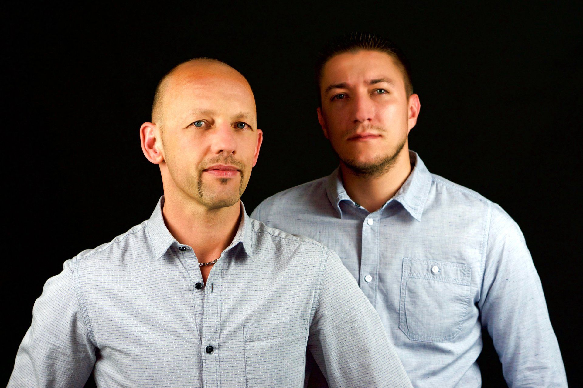 Zwei Männer stehen nebeneinander vor einem schwarzen Hintergrund.