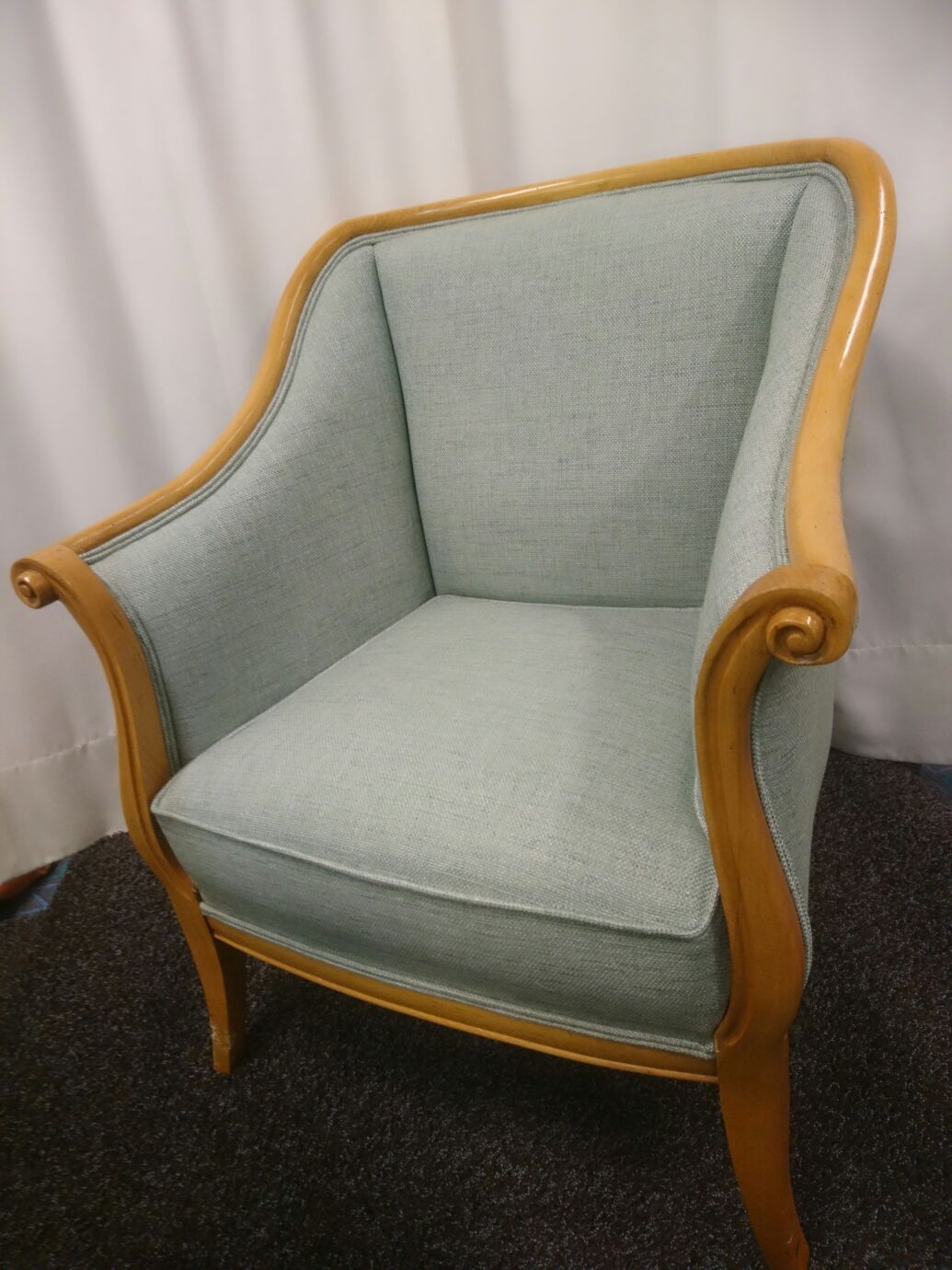 Ein blauer Stuhl mit Holzrahmen steht auf einem schwarzen Teppich