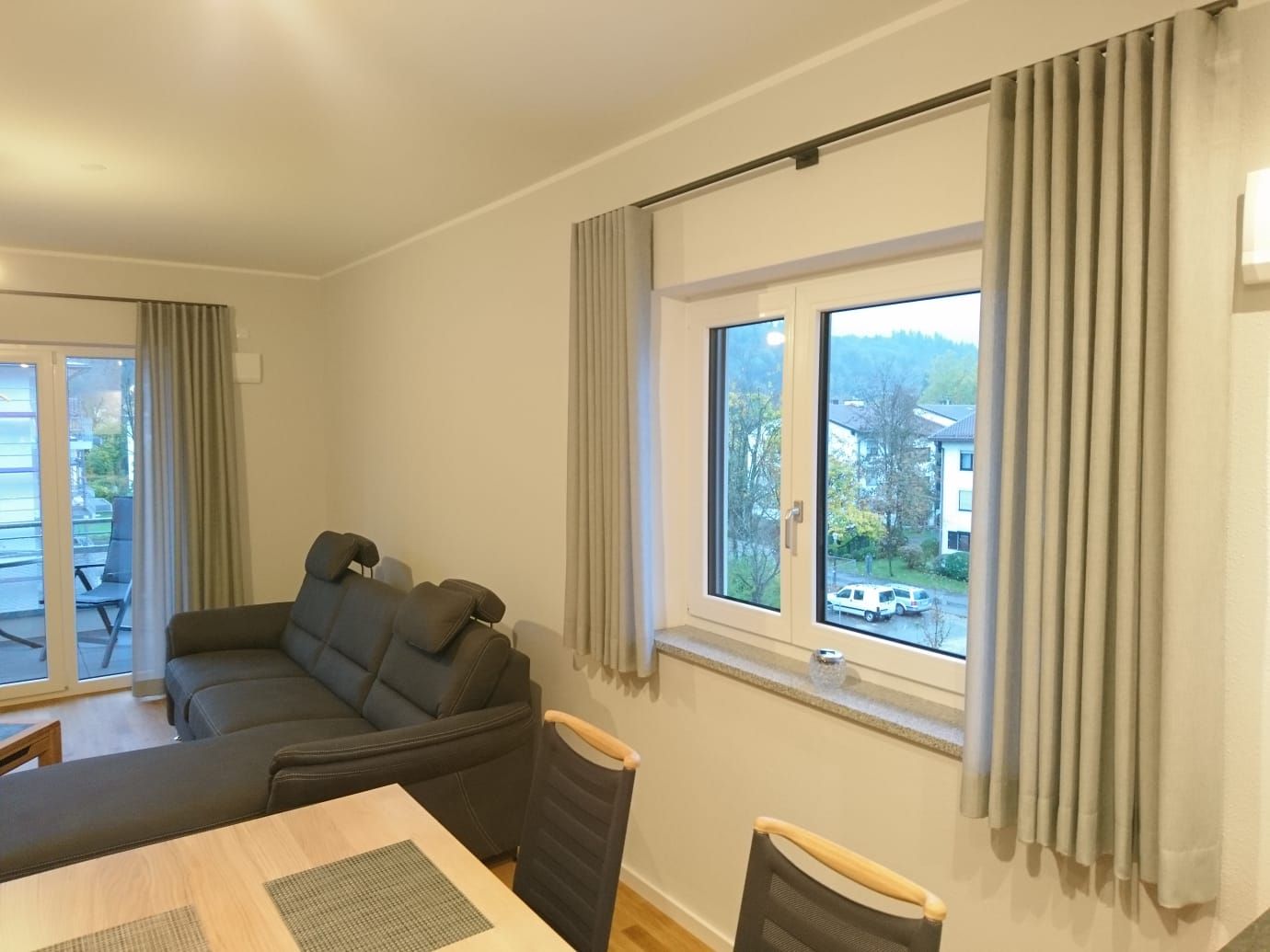 Ein Wohnzimmer mit Couch, Tisch, Stühlen und zwei Fenstern.