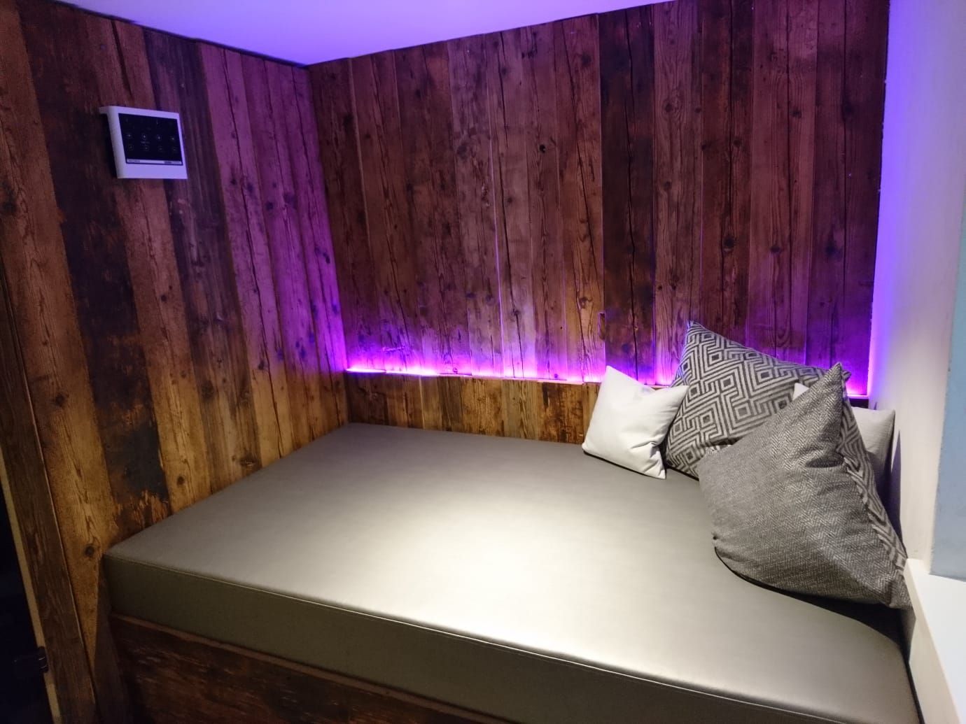 Ein Bett in einem Zimmer mit Holzwänden und violettem Licht.