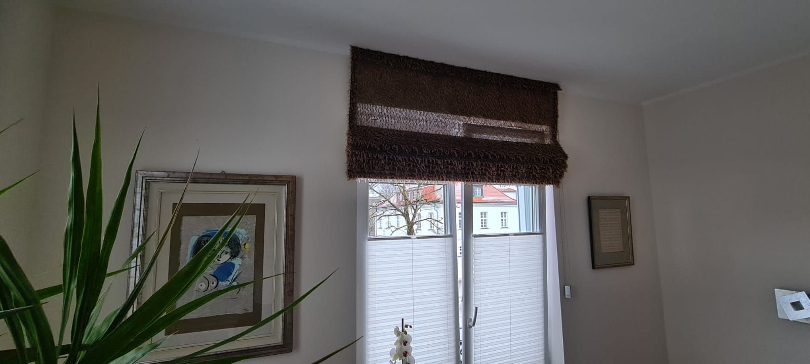 Ein Wohnzimmer mit einem großen Fenster und einer Pflanze davor.