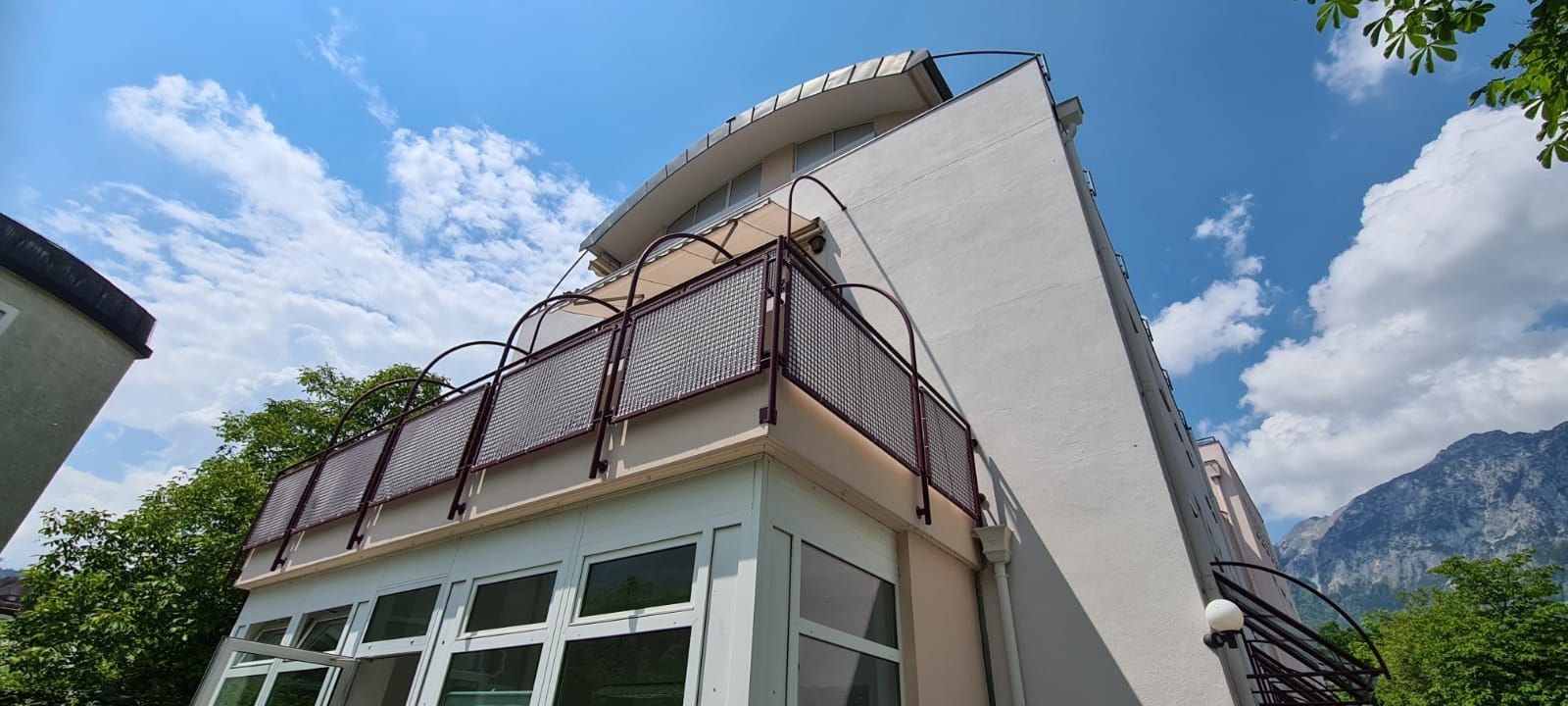 Ein großes weißes Gebäude mit einem Balkon und Bergen im Hintergrund