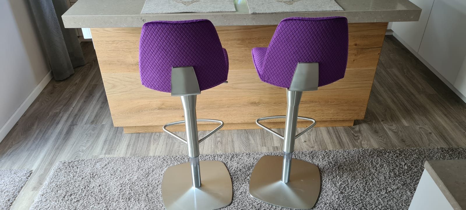 Zwei violette Barhocker stehen vor einer Holztheke.