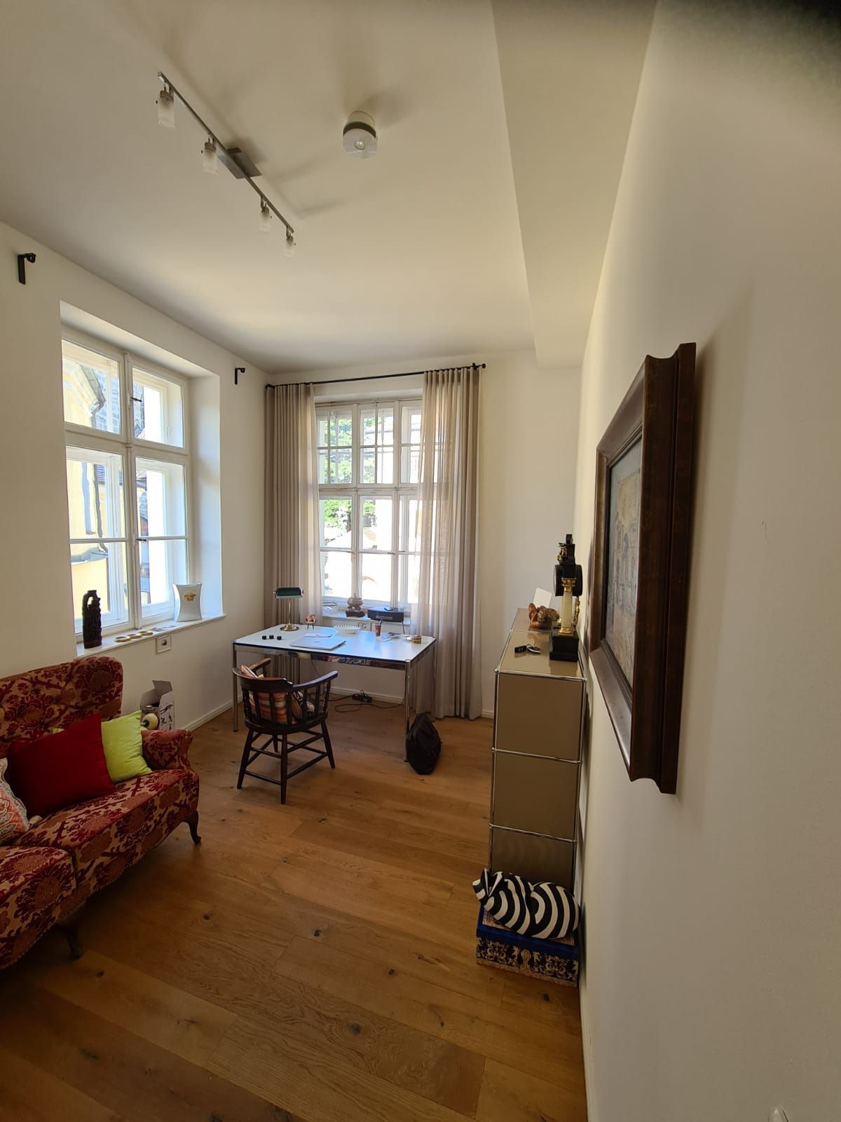 Ein Wohnzimmer mit Couch, Schreibtisch, Sessel und einem Bild an der Wand.