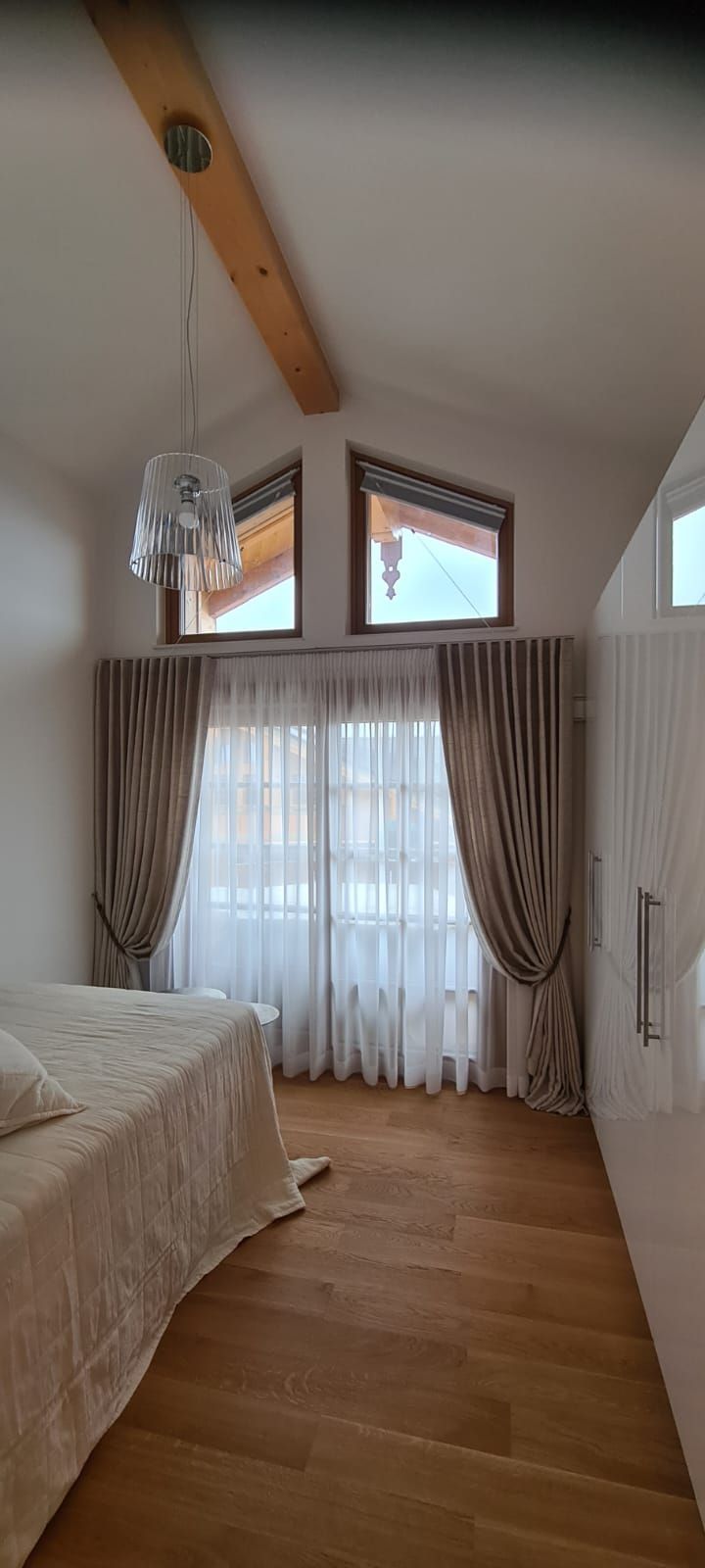 Ein Schlafzimmer mit einem Bett, Vorhängen und zwei Fenstern.