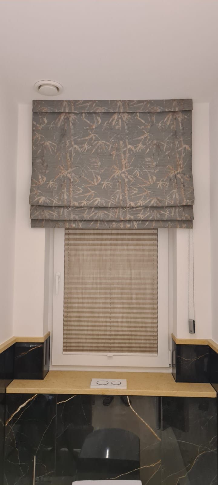 Ein Fenster mit einem Raffrollo und einem Schreibtisch davor.