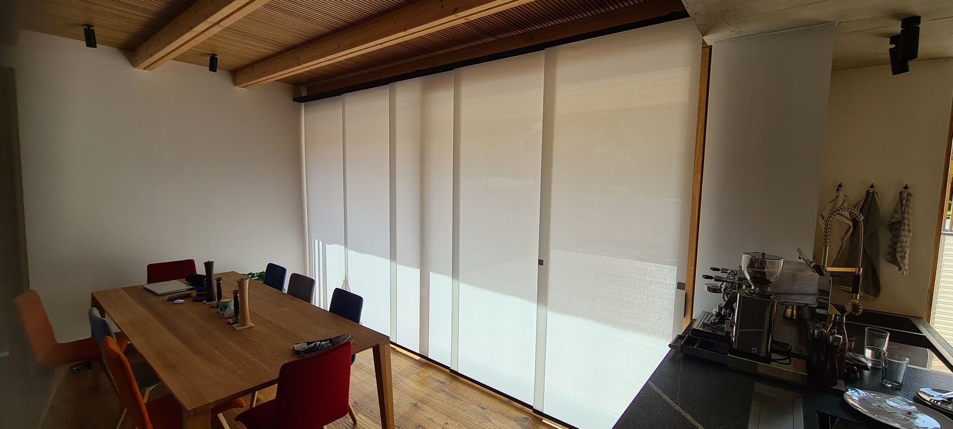 Ein Esszimmer mit einem Holztisch und Stühlen und weißen Jalousien an den Fenstern.