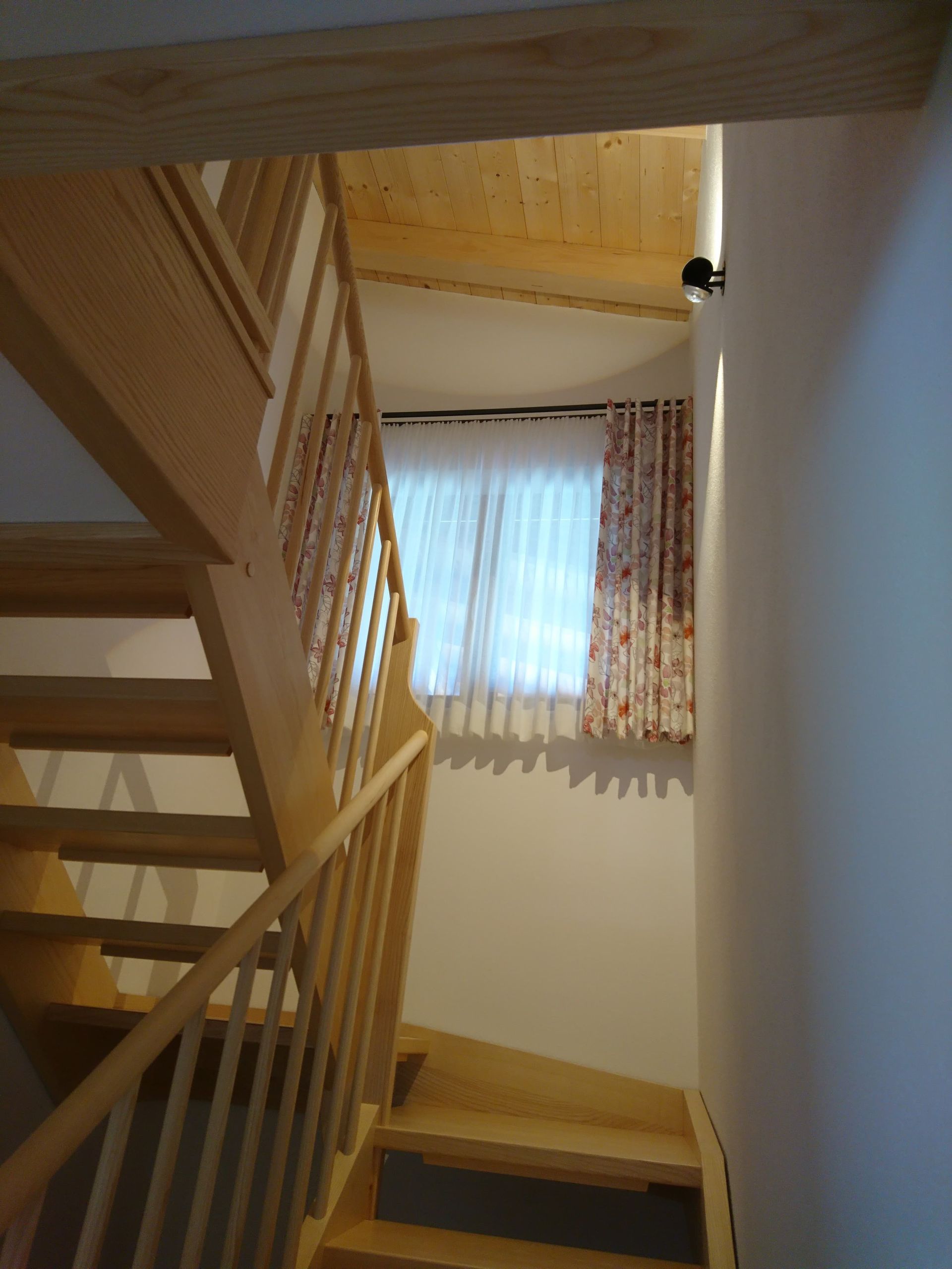 Eine Holztreppe, die zu einem Fenster mit Vorhängen führt