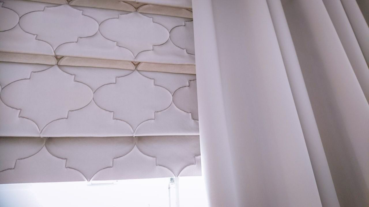 Eine Nahaufnahme eines Fensters mit einem Raffrollo und weißen Vorhängen.