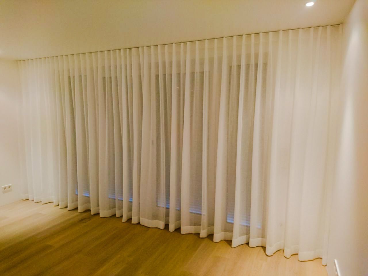 Ein Zimmer mit weißen Vorhängen und Holzboden.