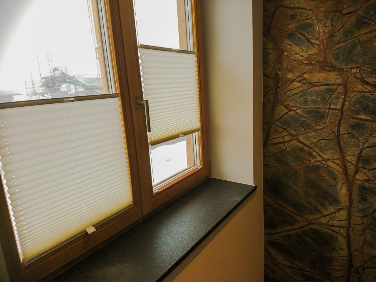 Auf einem Fensterbrett steht ein Fenster mit Plissees.